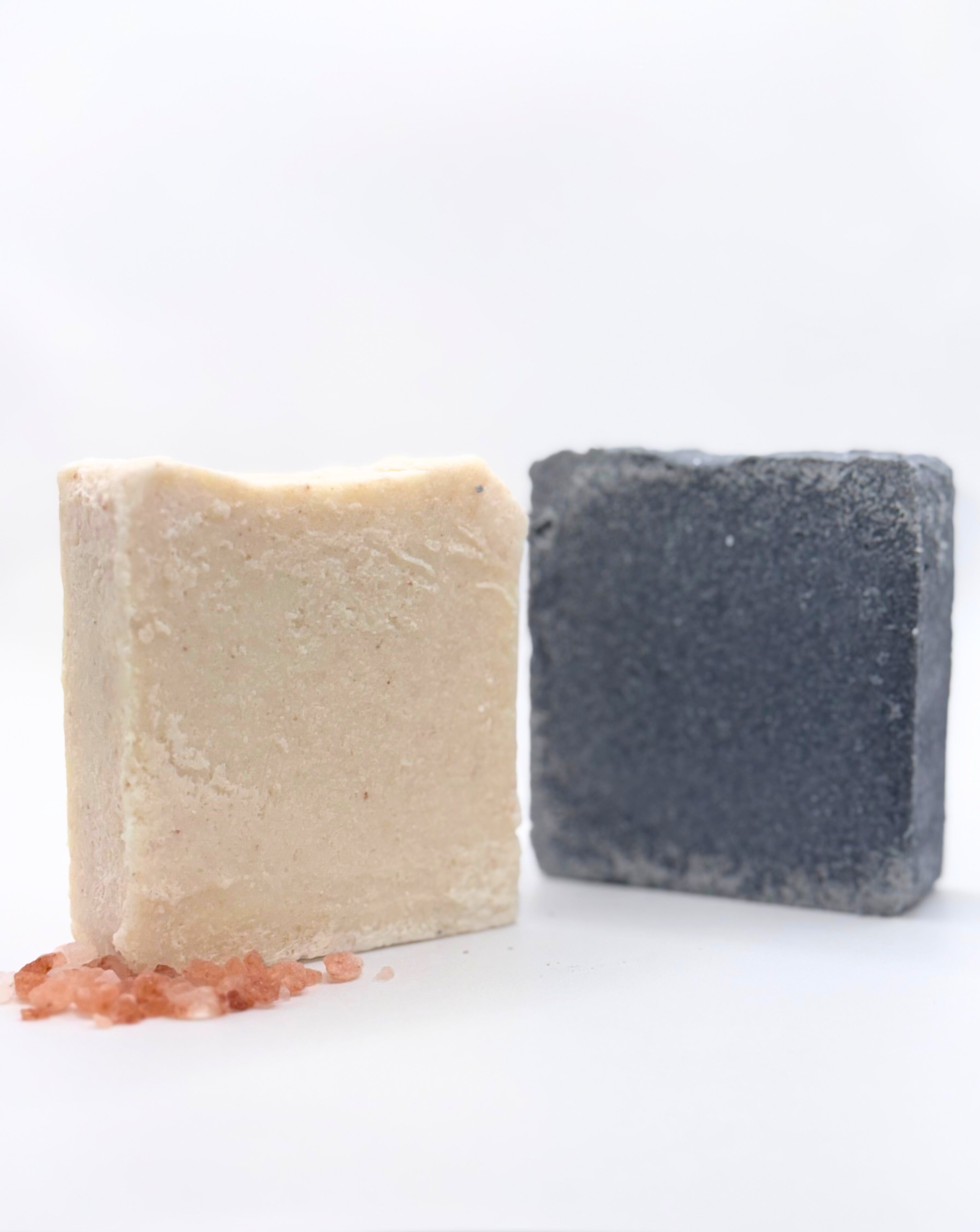 Two soap bars, one beige and one gray, on a white surface.